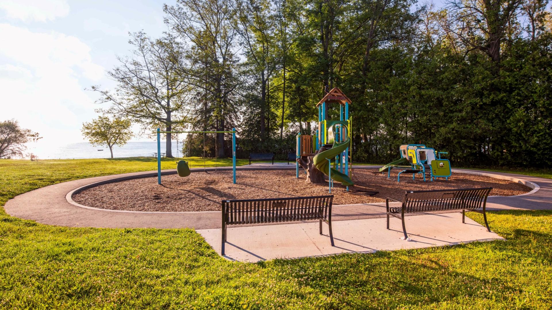 a park play ground with two benches surrounded by trees and grass