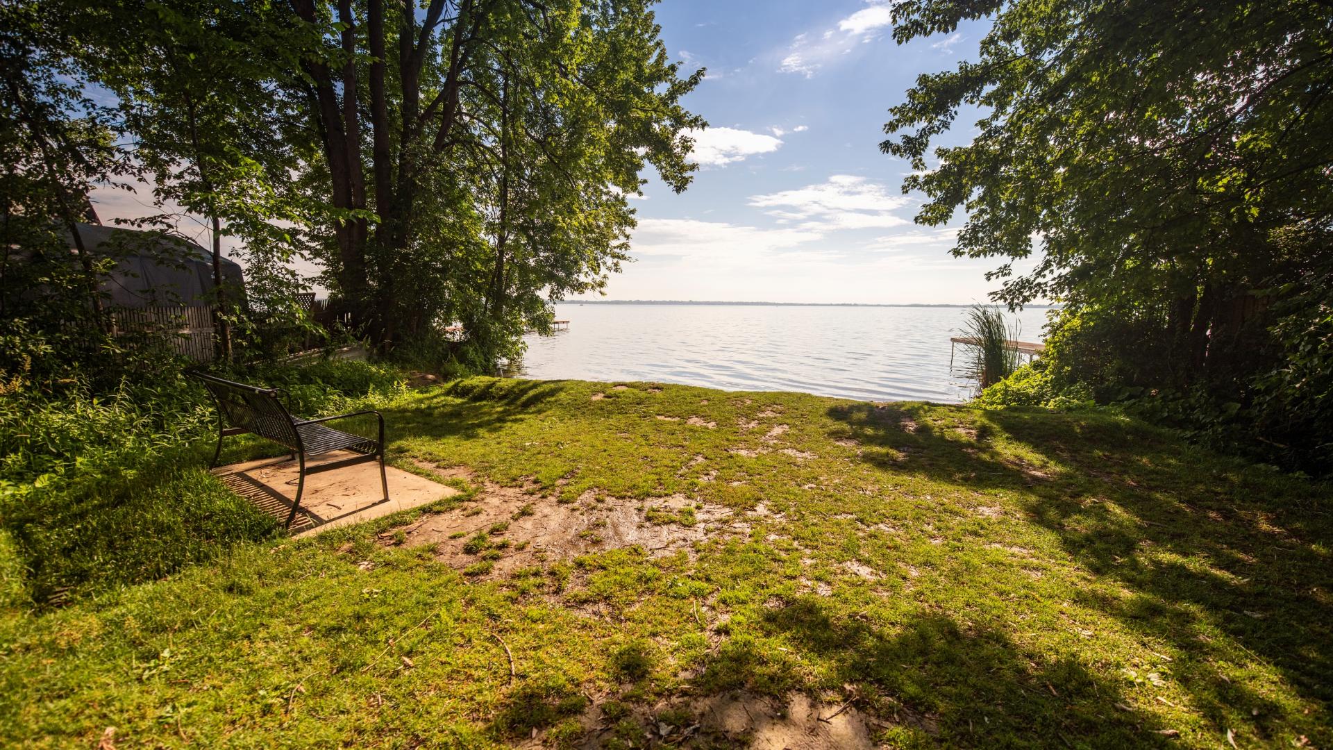 Bench in a grassy nook surrounded by lush trees to either side and a small beach directly in front