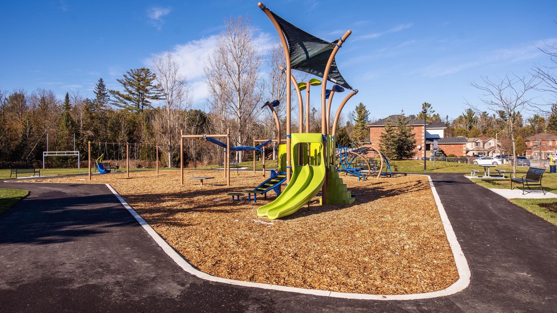 Modern children's playground with slides, swings, and other elements and a football field in the background