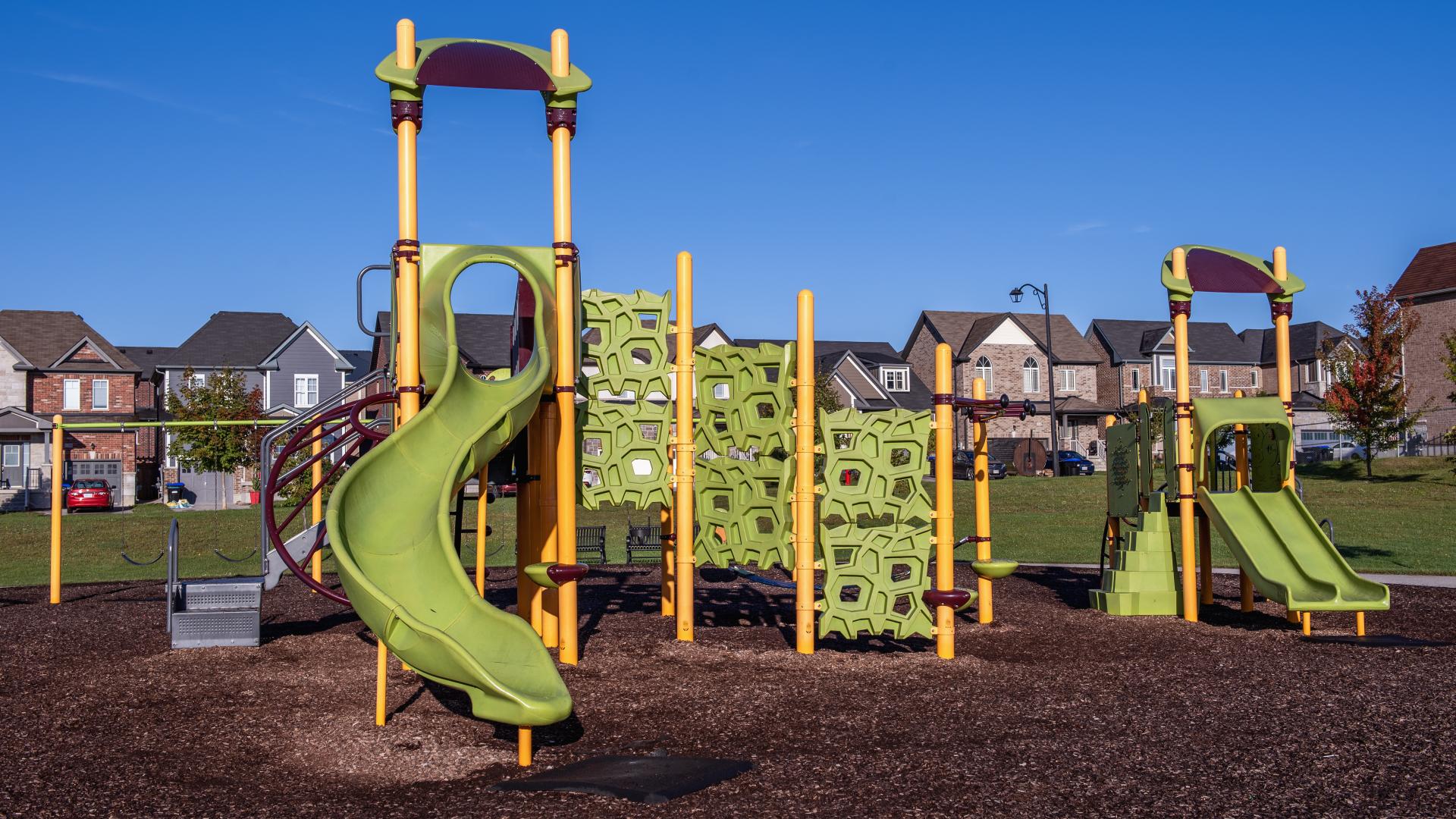 Modern children's playground with slides, climbing structures, and other elements and suburban houses in the background