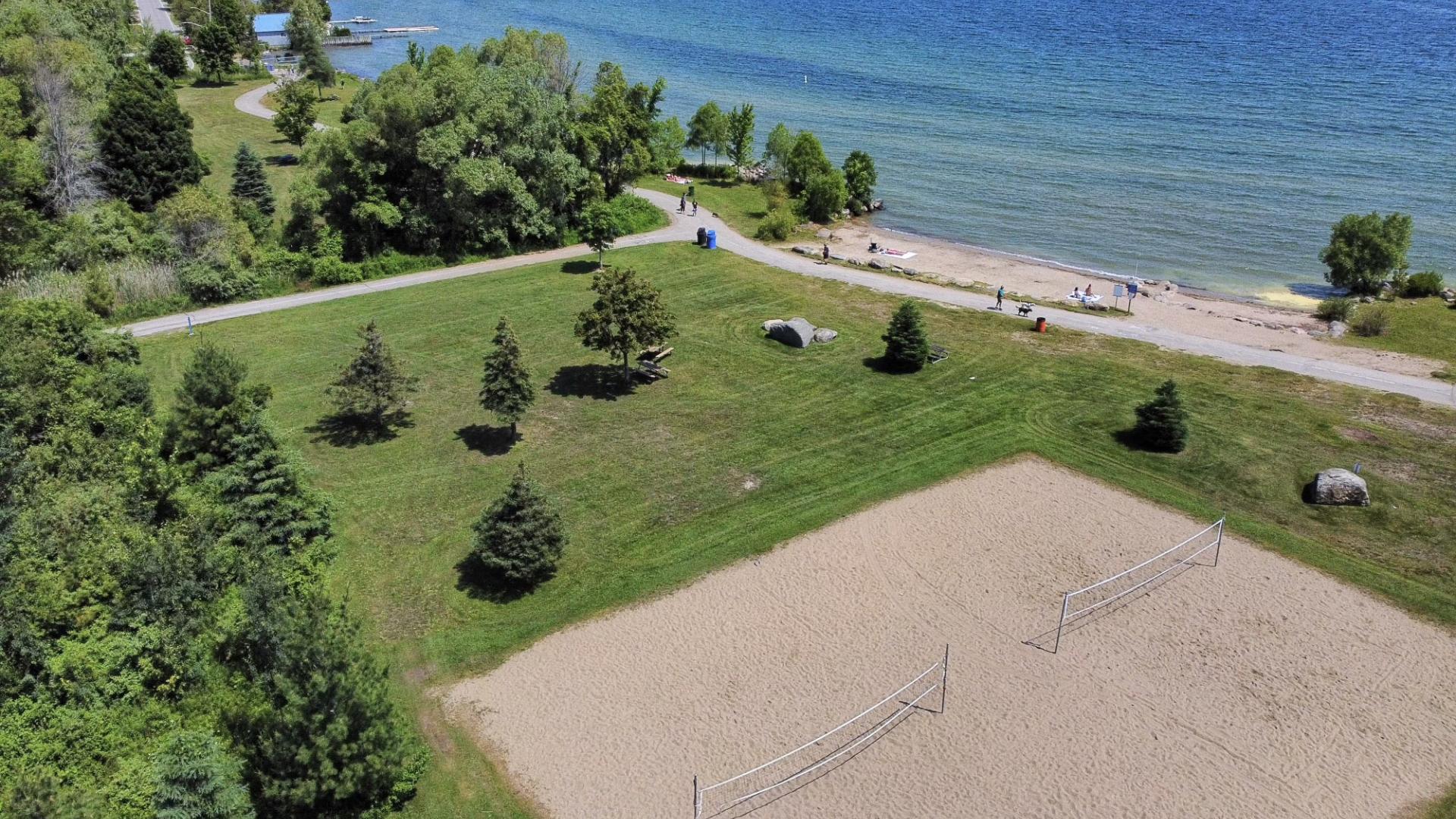 Arial view of two beach volleyball courts in a grass field with trees next to a lake