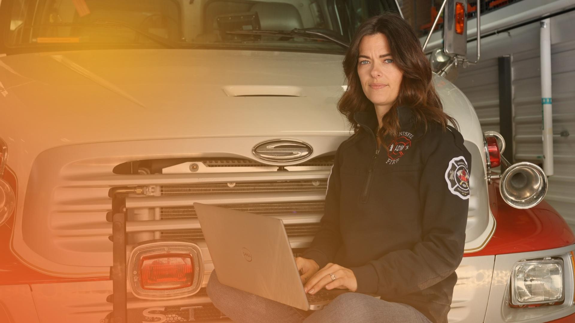 Woman with a laptop sitting on top of a fire truck