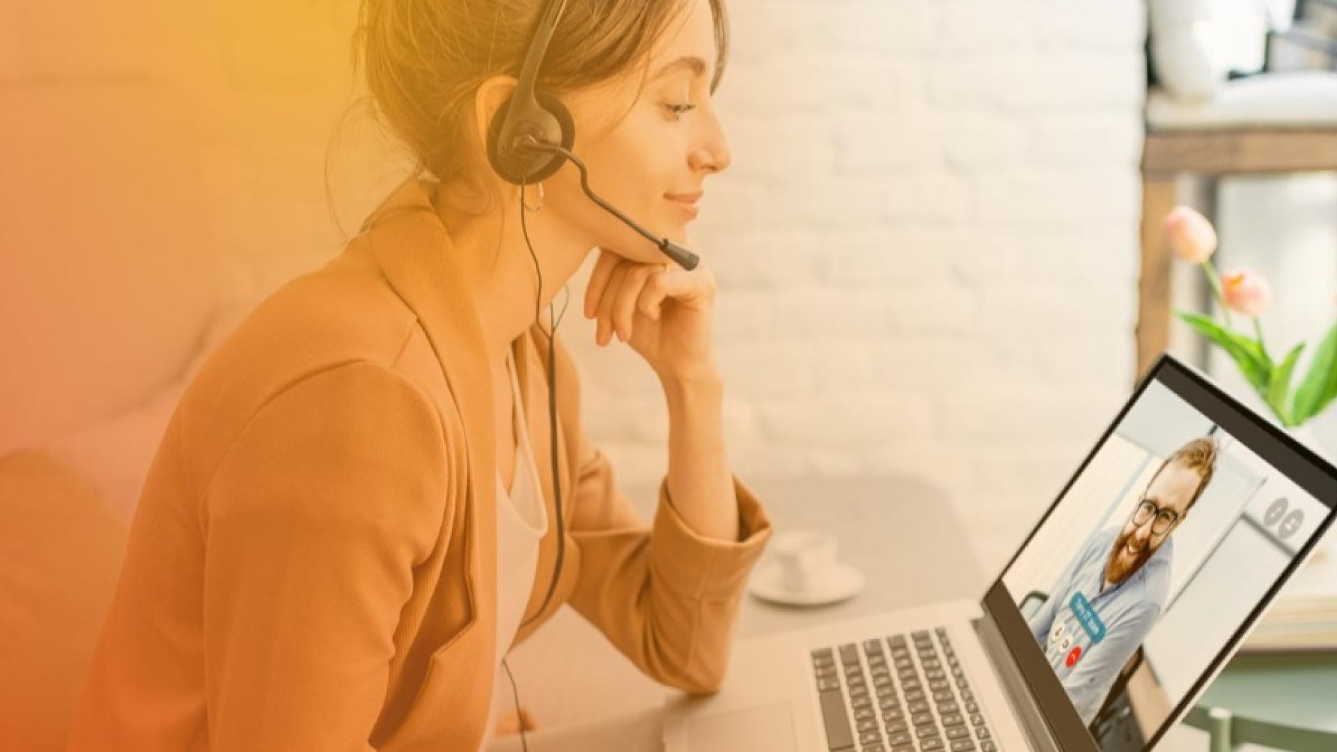 Woman with headset smiling at laptop during virtual meeting