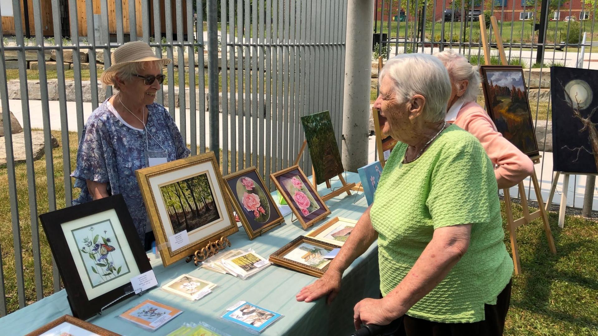 Seniors at outdoor art show, talking to artist and looking at art