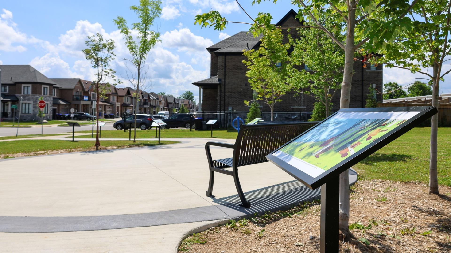 Paved path through McNeil Park with small trees and benches on either side with storyboards