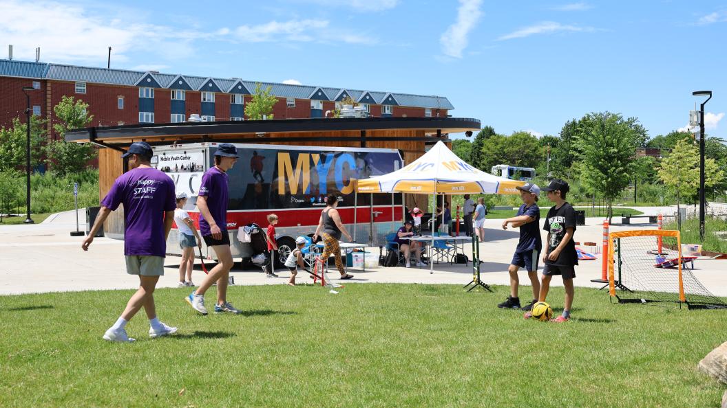 Two youth employees kicking soccer ball with kids at mobile youth centre