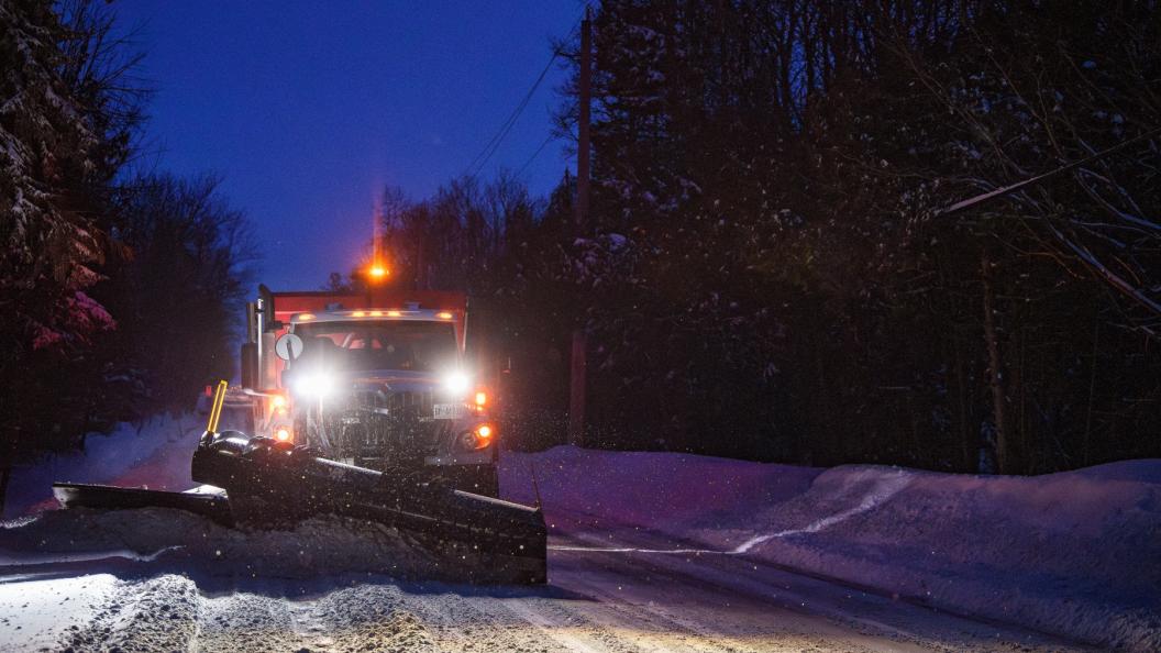 Snowplow pushing snow aside on rural road at night