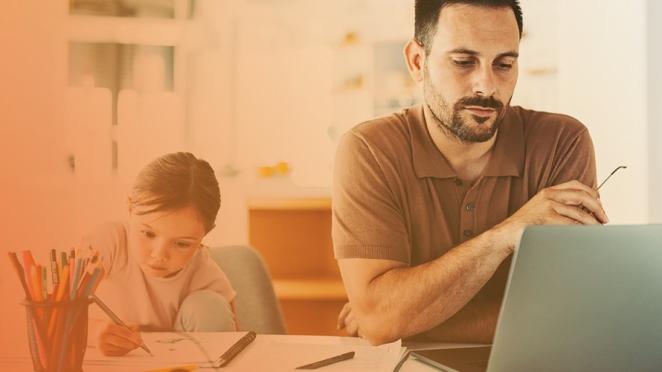 Man on laptop working while child colours on pad of paper next to him on table