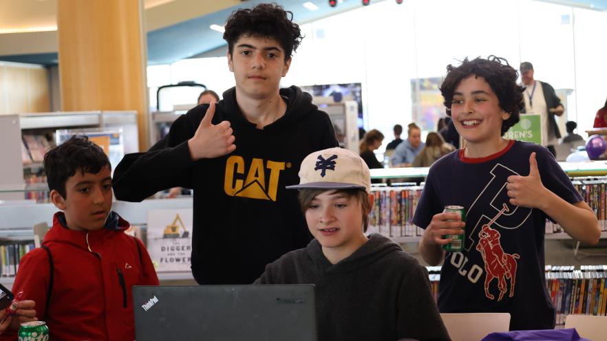Four teen boys looking at a laptop screen and smiling