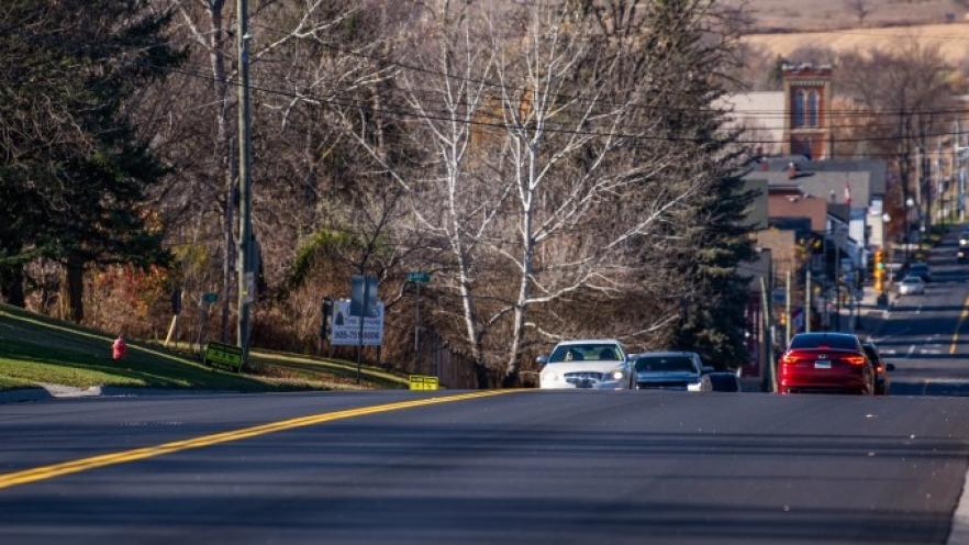 Quiet suburban street with cars and trees lining both sides.