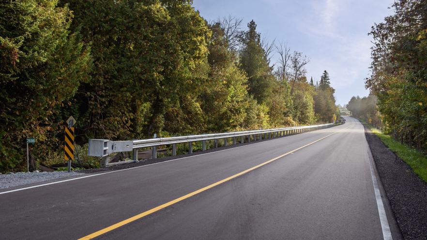 Two lane road going across a forested area with freshly laid asphalt and road lines