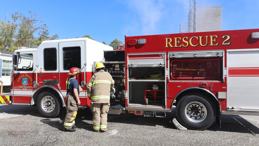 Two firefighters standing by fire truck