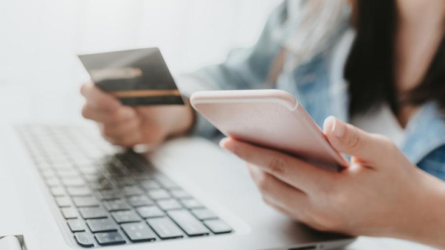 Close-up of female's hand holding credit card using smartphone to pay something online.