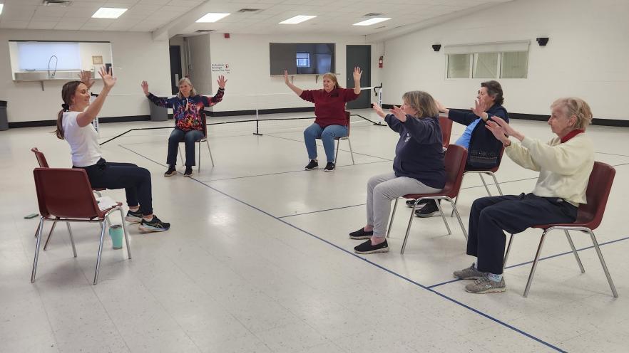 Senior participants following an instructor for dancing while sitting down