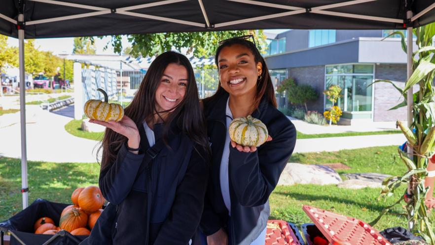 Two female staff members smiling while holding pumpkins