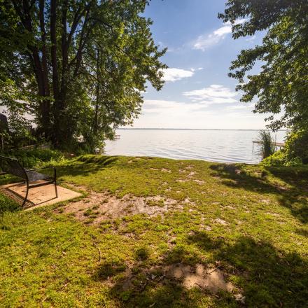 Bench in a grassy nook surrounded by lush trees to either side and a small beach directly in front