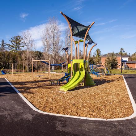 Modern children's playground with slides, swings, and other elements and a football field in the background
