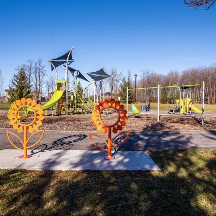 Bike racks in the shape of two sunflowers in the foreground; behind is a children's playground with slides, swings, climbing structures, and other elements