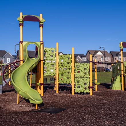 Modern children's playground with slides, climbing structures, and other elements and suburban houses in the background