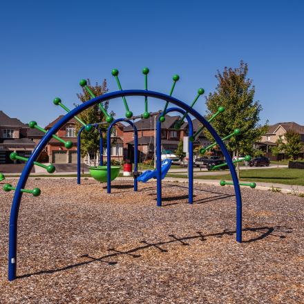Spiraling free standing monkey bar in a children's playground and suburban houses in the background