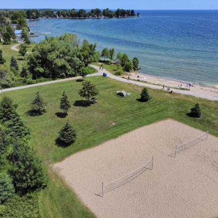 Arial view of two beach volleyball courts in a grass field with trees next to a lake