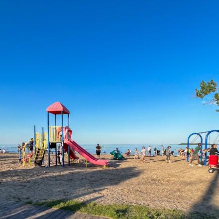 Kids using playground and swing set at a beach park on a sunny day
