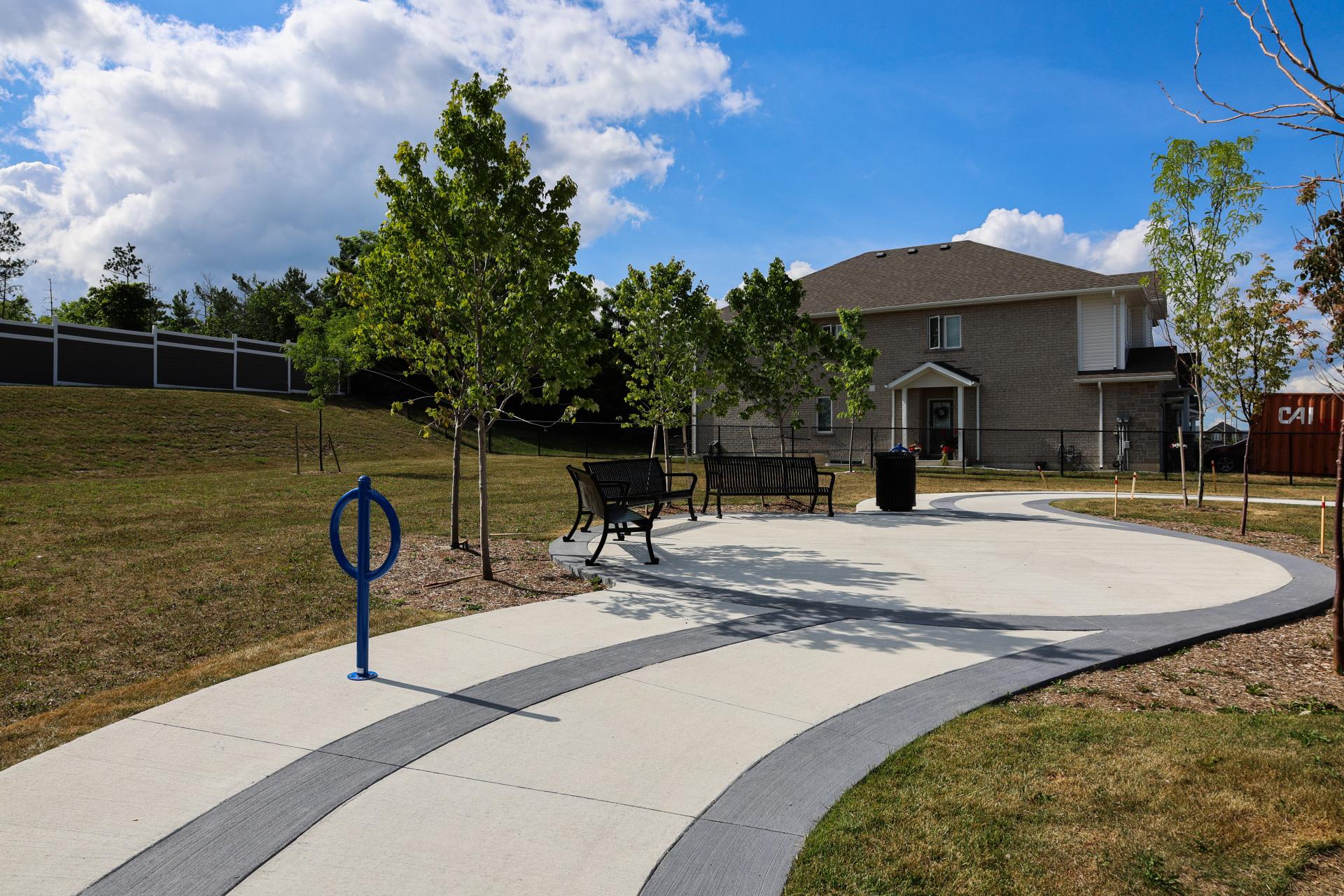 Wide paved trail across a grassy area with benches, bike racks, and trees