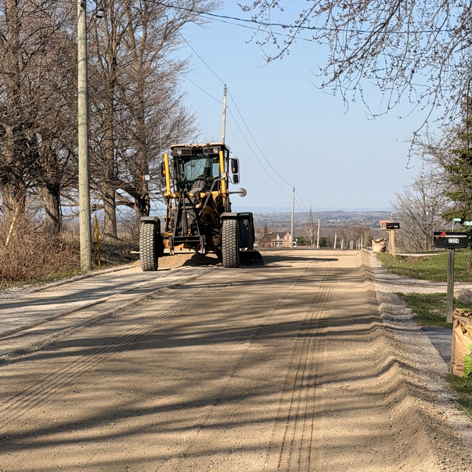 Grader spreading material on gravel road in Innisfil